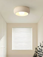 Beige Clérachic ceiling light in a bare, bright room with a window covered by white blinds and a plant at the corner.