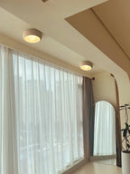 Two beige Clérachic ceiling lights along a sunlit room with sheer curtains, an arched mirror and a plant by the window.