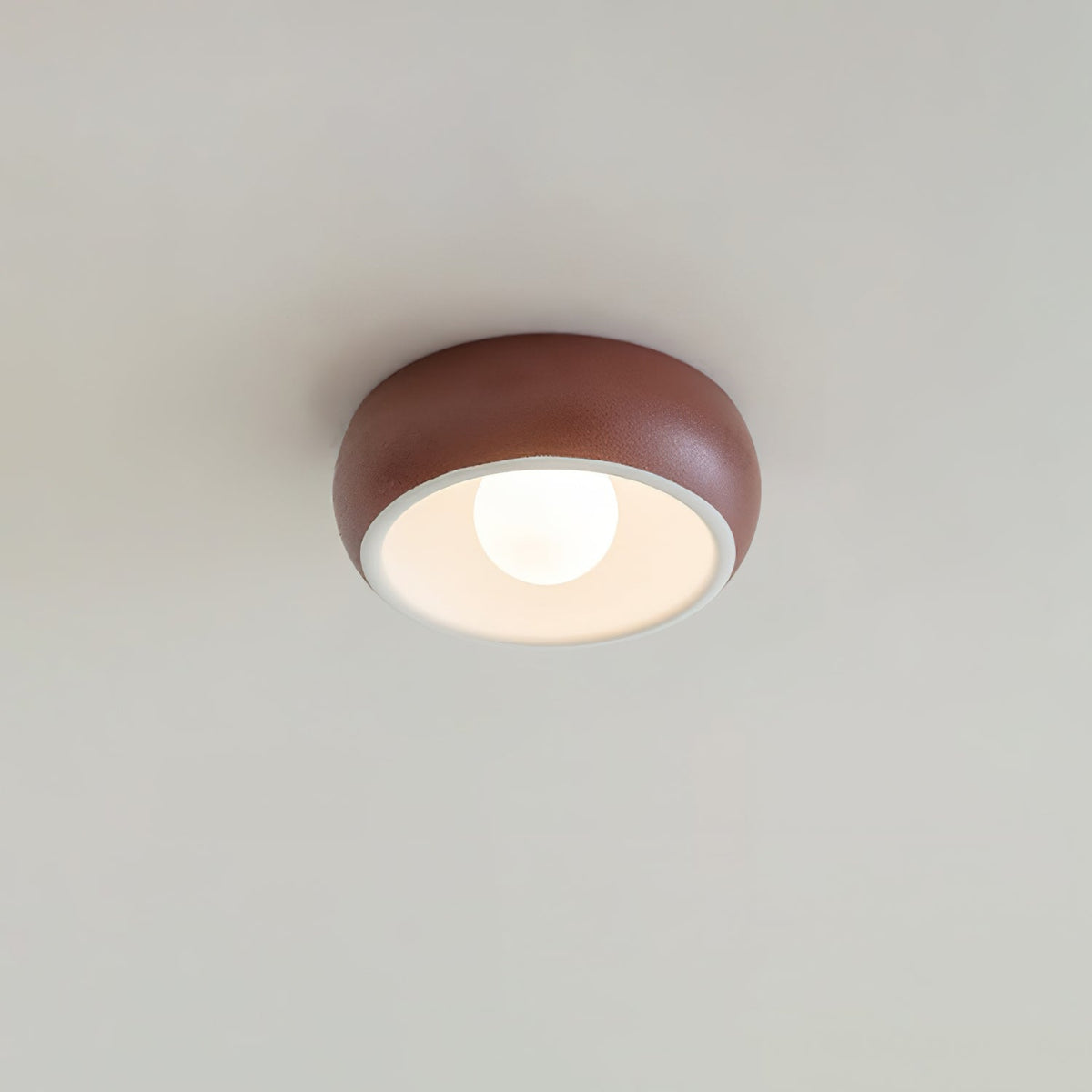 Red Clérachic ceiling light on a pale ceiling, a terracotta-red outer bowl around a white inner rim and a round bulb.