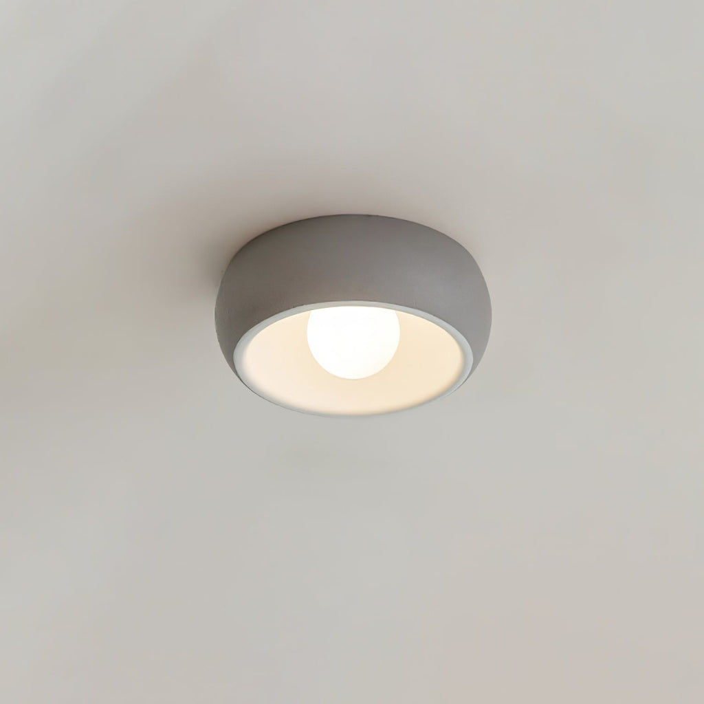 Close view of a grey Clérachic ceiling light on a pale grey ceiling, its white interior and round bulb lit.