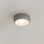 Close view of a grey Clérachic ceiling light on a pale grey ceiling, its white interior and round bulb lit.