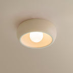 Beige Clérachic ceiling light close up on a warm cream ceiling, its pale bowl glowing around the round bulb.