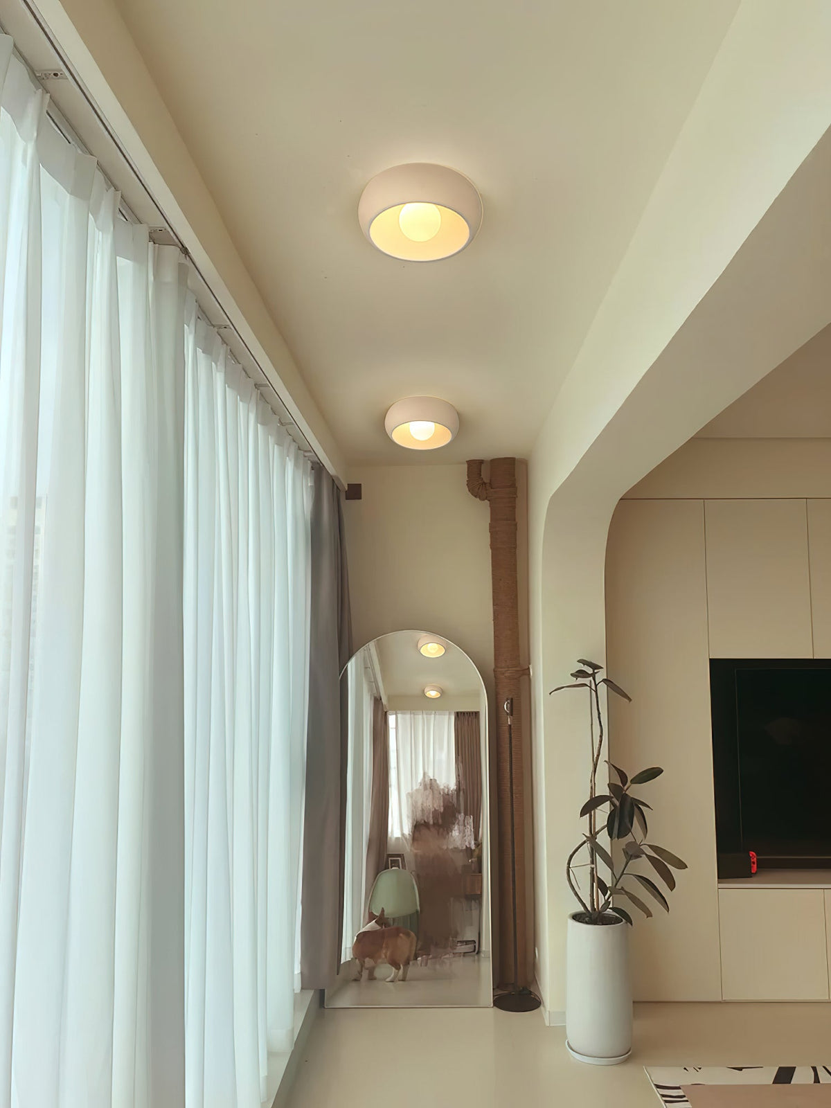 Long view down a curtained hallway, with two beige Clérachic ceiling lights, an arched mirror and a tall plant at the end.
