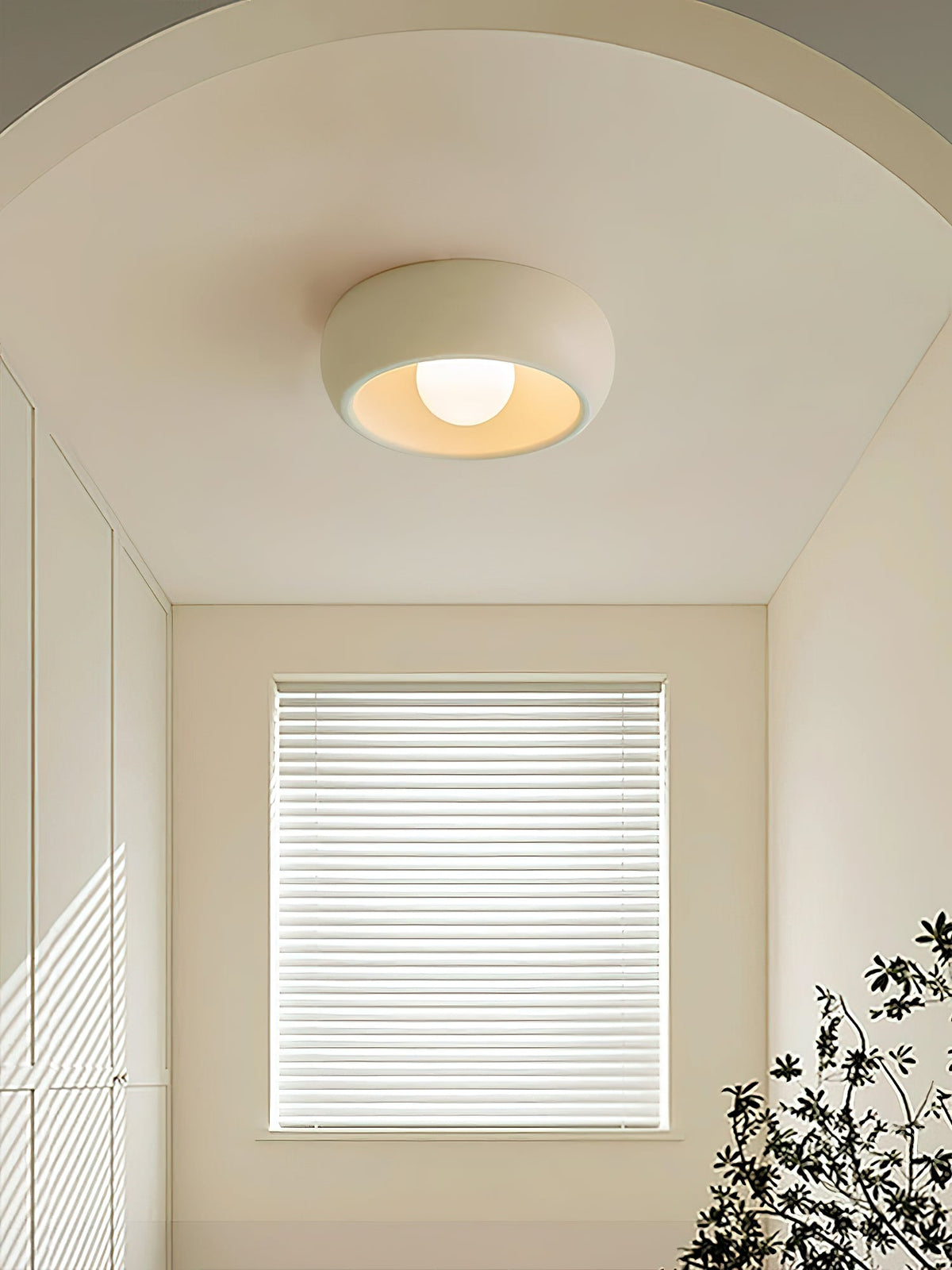 Beige Clérachic ceiling light on an arched ceiling above a small room with a blinded window and a plant at the right.