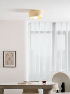 Beige Clérachic ceiling light in a white dining room, glowing above an oval table with a glass and a book on top.