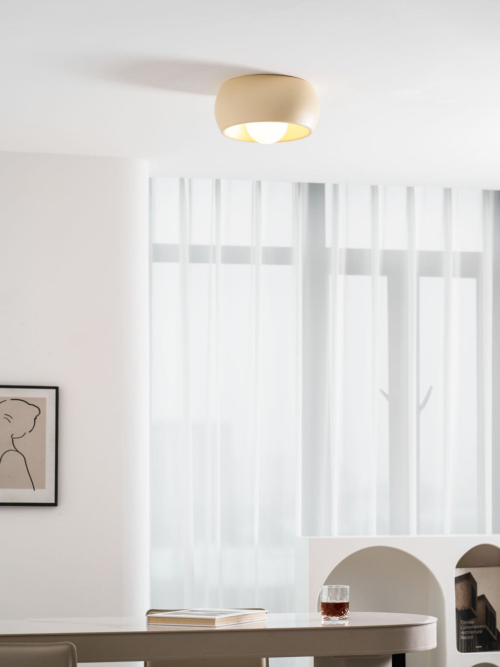 Clérachic ceiling light lit in a bright white room, near sheer curtains and an arched cream shelf unit at the right.