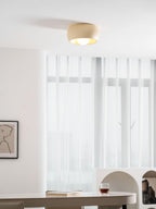 Clérachic ceiling light lit in a bright white room, near sheer curtains and an arched cream shelf unit at the right.