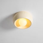 Angled view of this beige Clérachic ceiling light, lit, showing the rounded outer bowl and the glowing yellow interior.