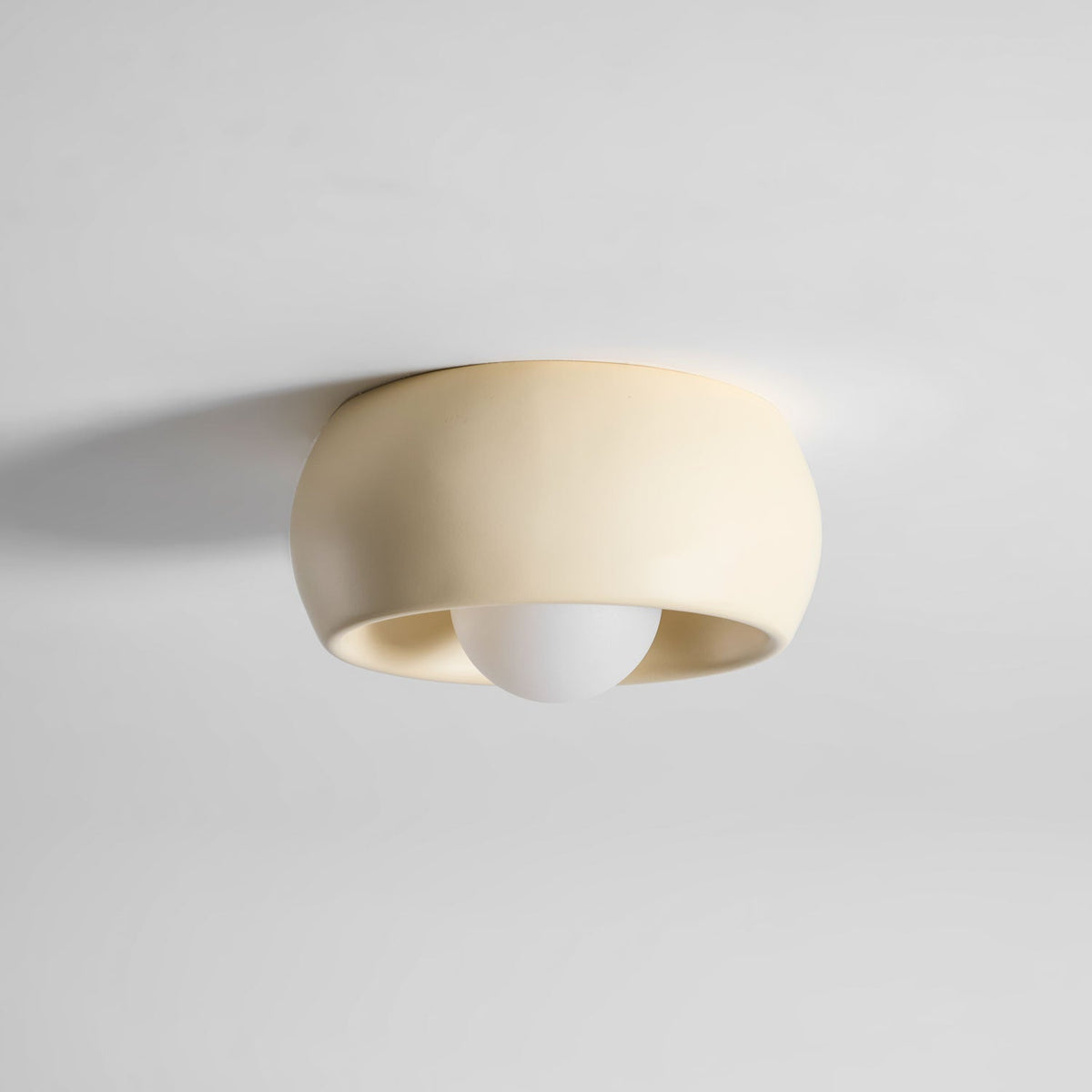 Side view of this beige Clérachic ceiling light, the round bulb just visible below the rim of its shallow bowl.