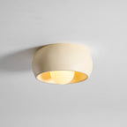 Low, angled view of this lit beige Clérachic ceiling light, with warm light showing along the inside of the bowl.