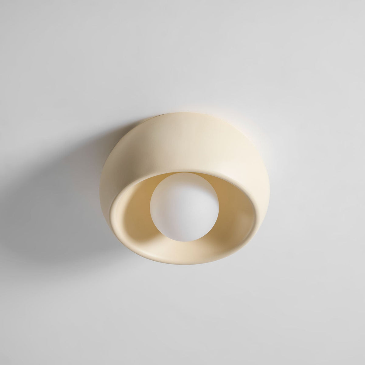 Angled view of this cream Clérachic ceiling light, its round white bulb deep inside the soft-edged bowl on a pale surface.