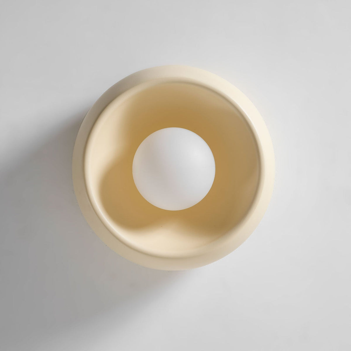 Close, front-on view of this cream Clérachic ceiling light, a smooth bowl surrounding a round white bulb.