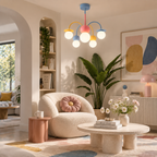 Pastel globe chandelier from Clérachic above a cream boucle armchair and a low stone coffee table in a living room with a large plant.
