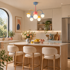 Coloured-arm Clérachic chandelier over a light wood kitchen island with cream stools, lemons in a bowl and a tall arched window beyond.