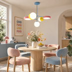 A Clérachic chandelier with pink discs and white globes hangs over a round wooden table with pink and blue upholstered dining chairs.