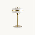 Cut-out view of a Clérachic table lamp with a stacked white glass shade, a brass band and a slim gold stem on a round base, on white.