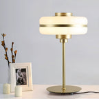 Clérachic table lamp on a white console beside a framed photo, small candles and bare branches, its white shade and gold stem in view.