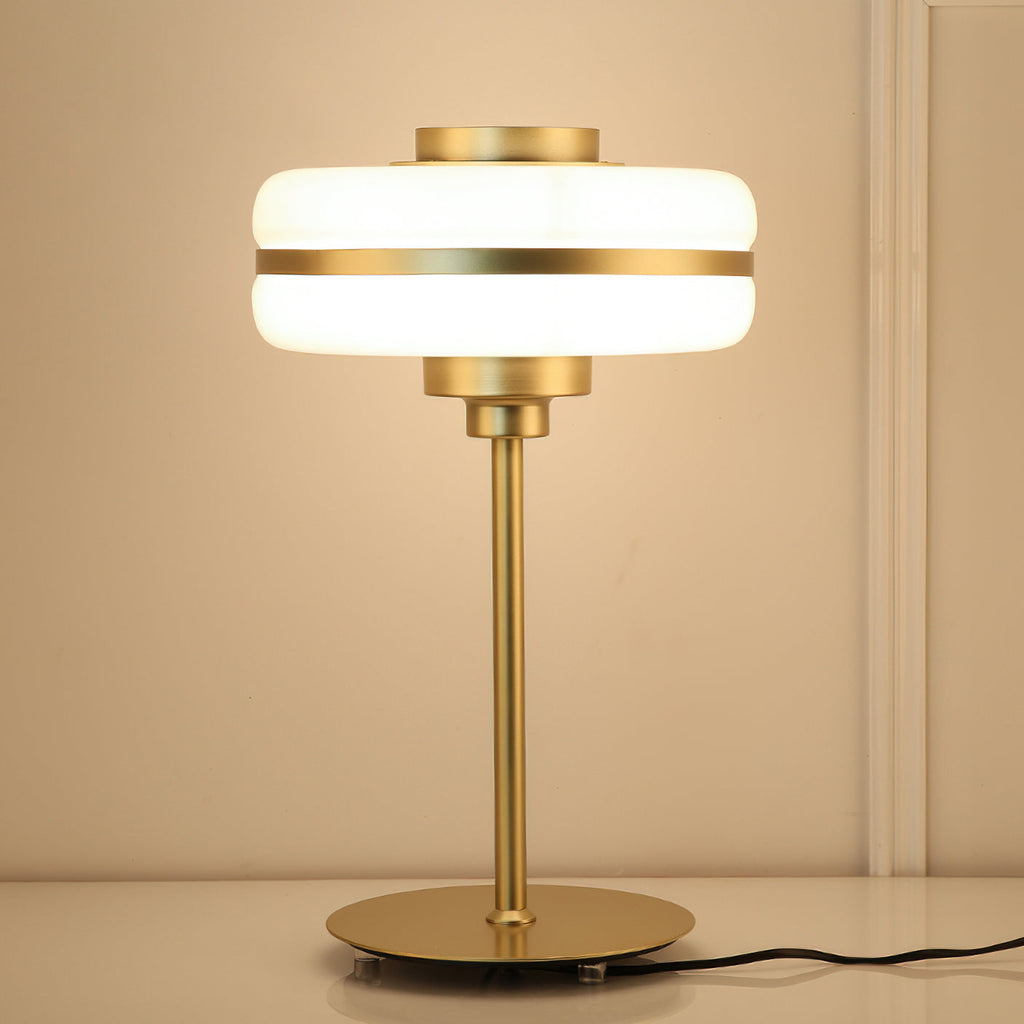 Warm light glows through the stacked white glass shade of this Clérachic table lamp, with its gold stem and flat round base.