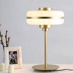 Clérachic table lamp lit beside a framed black and white photo and candles, its gold stem and round base clear against a grey wall.