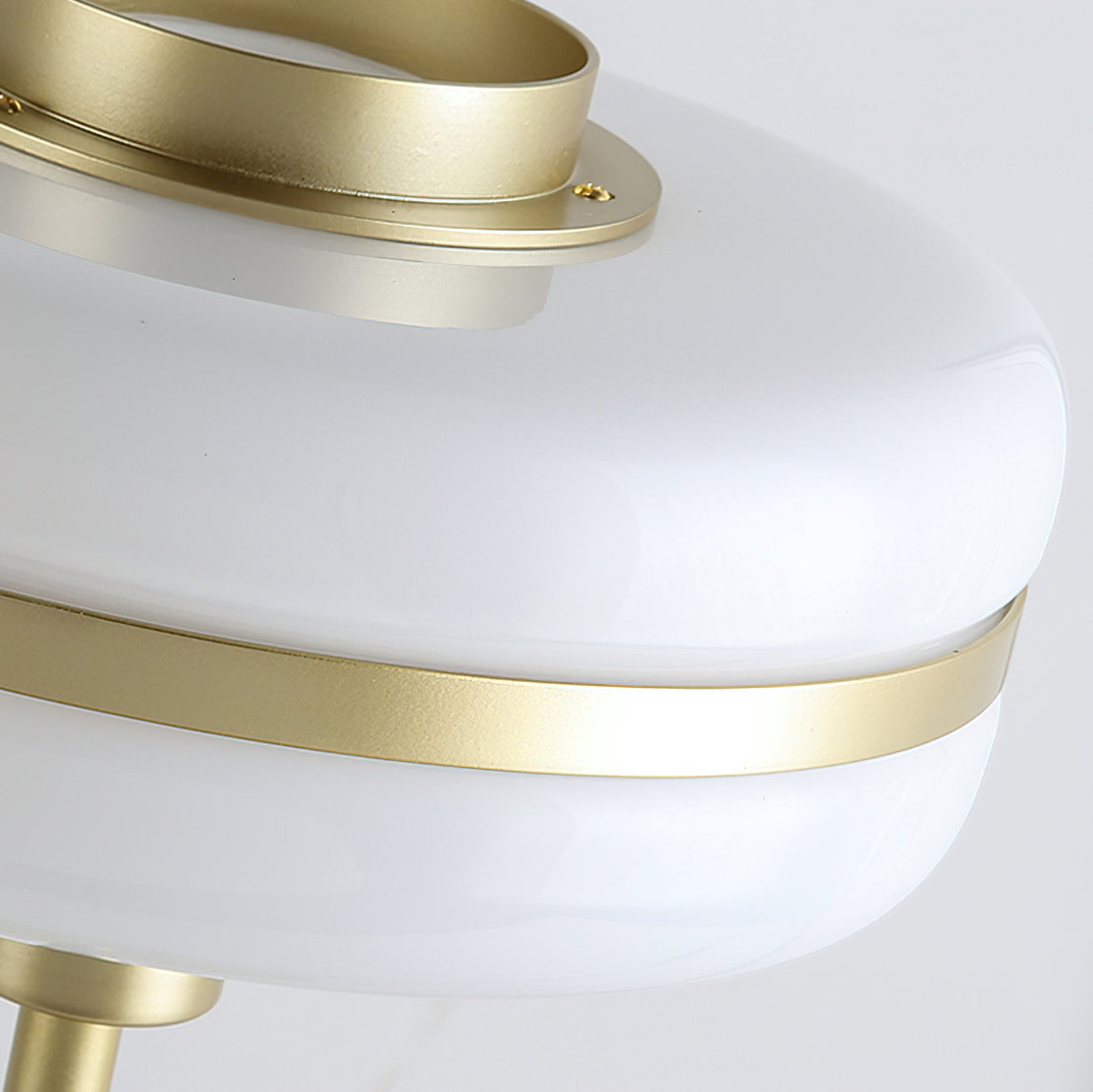 Close view of the white glass shade and the gold band with a small screw detail on this Clérachic table lamp.