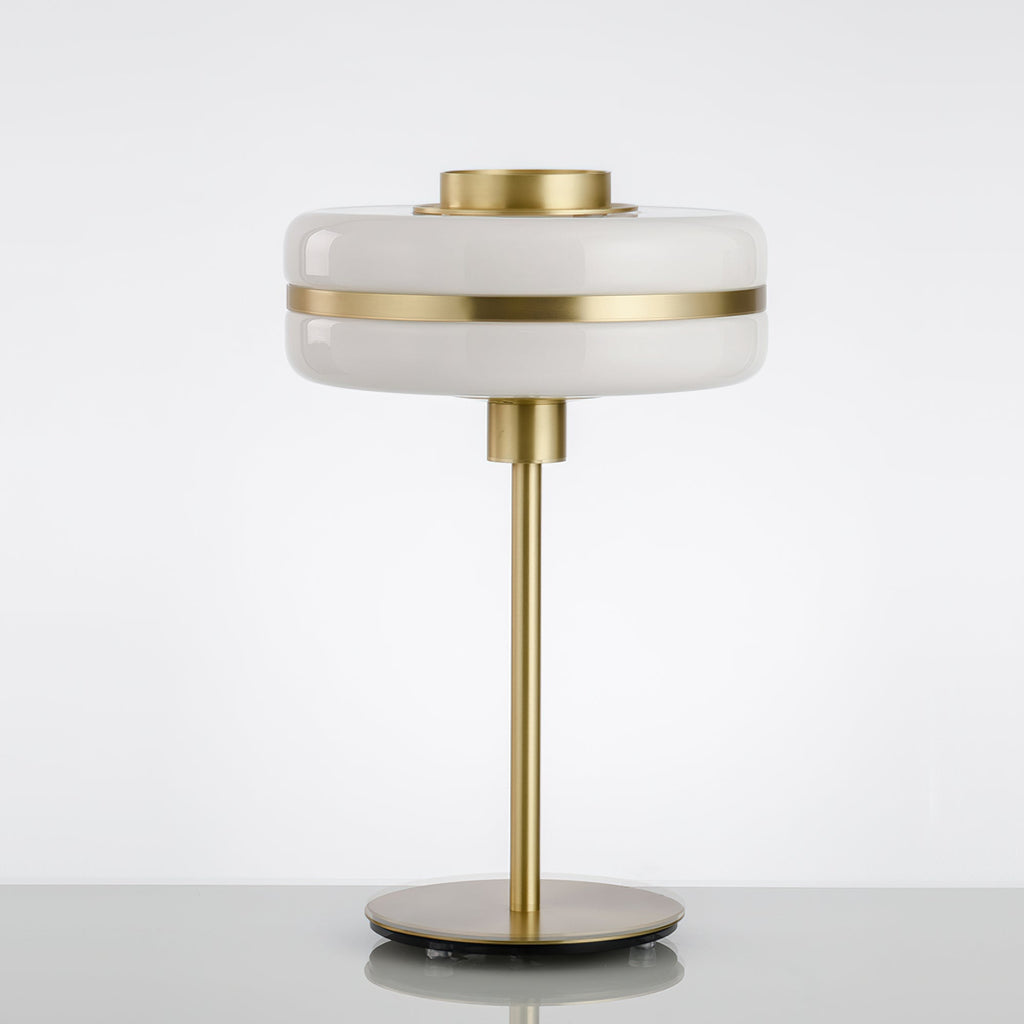 Unlit Clérachic table lamp with a white glass shade, gold band and slim gold stem on a pale surface against a soft grey backdrop.