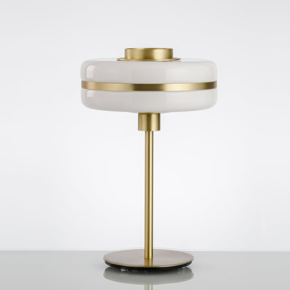 Unlit Clérachic table lamp with a white glass shade, gold band and slim gold stem on a pale surface against a soft grey backdrop.