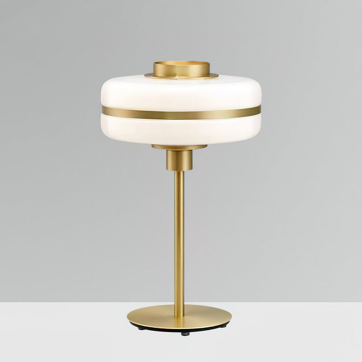 This Clérachic table lamp with an unlit white glass shade and a gold stem and round base stands against a plain grey wall.