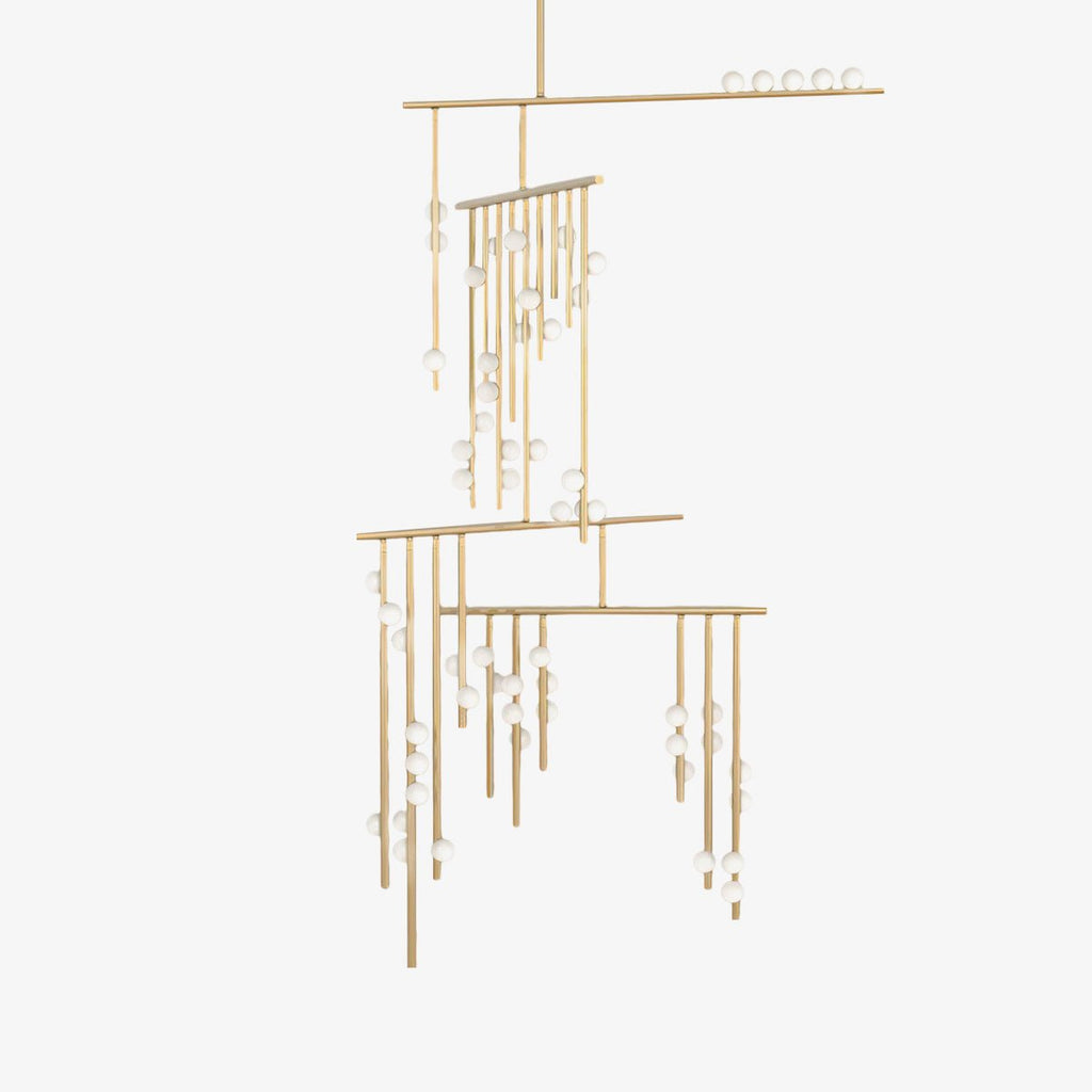 This Clérachic chandelier on a plain white backdrop, with brass rods hung at different heights and small white glass orbs along each one.