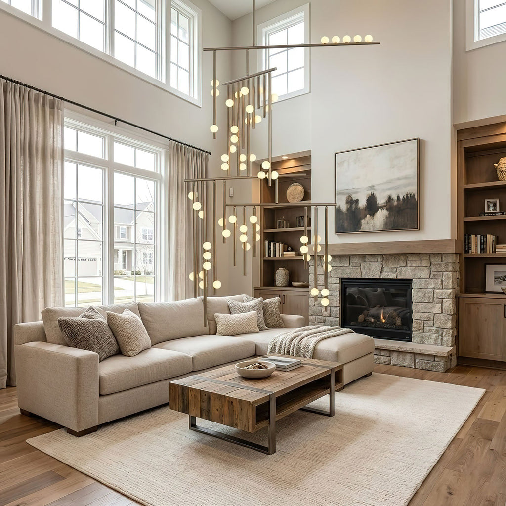Tall living room with a stone fireplace and cream sofa, where a Clérachic chandelier drops its lit white orbs down the full height of the space.