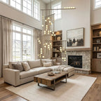 Tall living room with a stone fireplace and cream sofa, where a Clérachic chandelier drops its lit white orbs down the full height of the space.