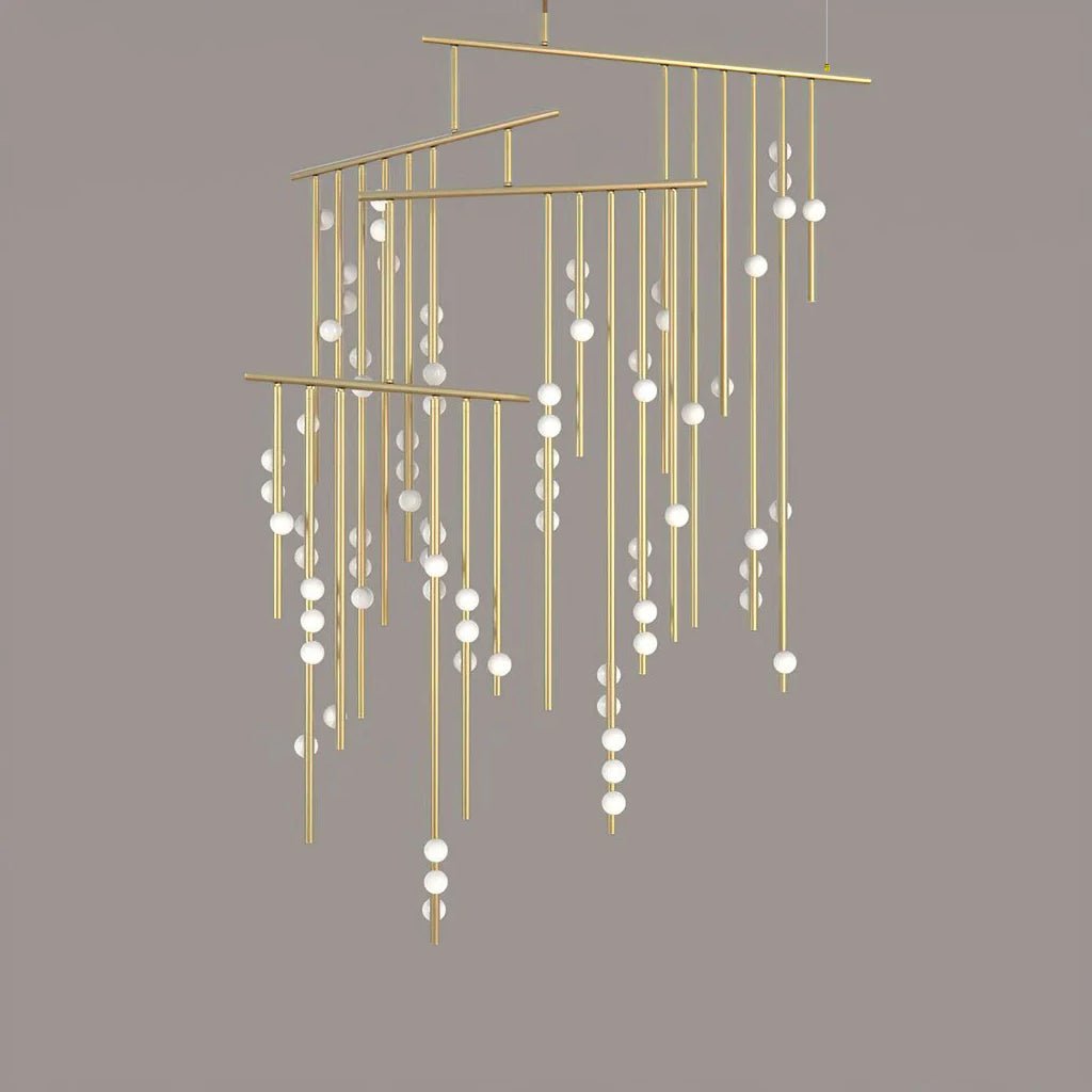 A Clérachic chandelier in brass with many tiers of drop rods and white orbs, on a taupe backdrop.
