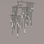 A black Clérachic chandelier with many tiers of drop rods and white orbs, on a taupe backdrop.