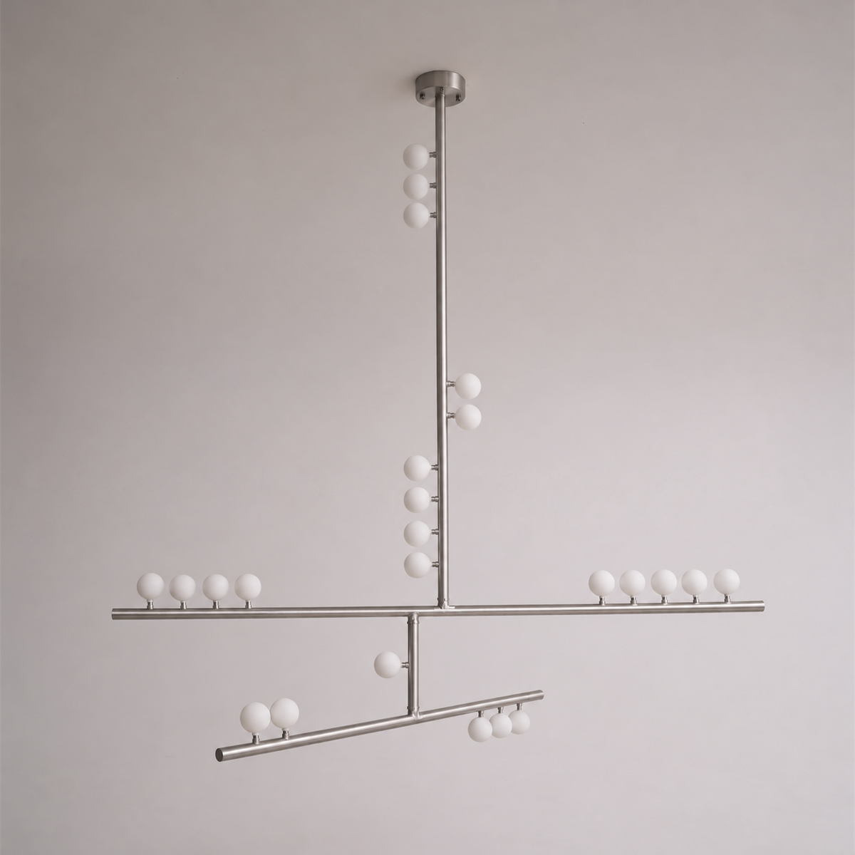 This Clérachic pendant in a nickel-toned finish, with crossed bars and white orbs, on a soft grey wall.