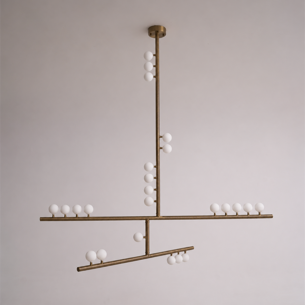 A Clérachic pendant in antique bronze, with a round ceiling plate and crossed bars, on a soft grey wall.