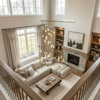 Looking down from a landing at a two-storey living room, a Clérachic chandelier hangs beside the high windows, its orbs glowing warm.