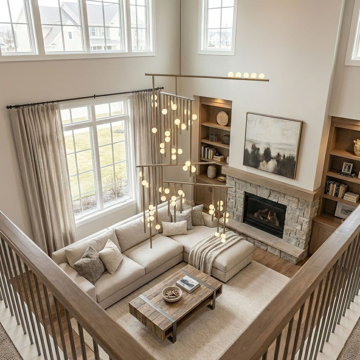 Looking down from a landing at a two-storey living room, a Clérachic chandelier hangs beside the high windows, its orbs glowing warm.