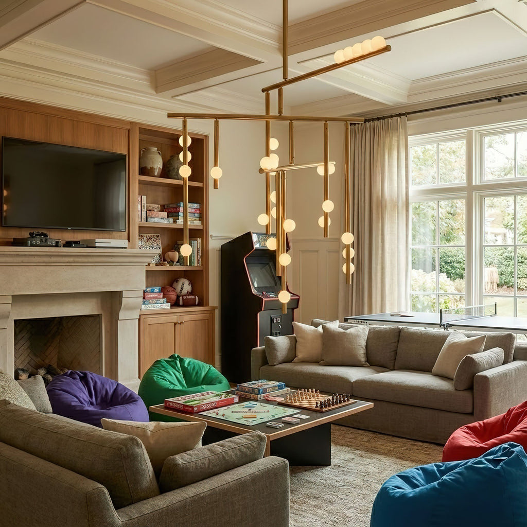 Lit orbs on a Clérachic chandelier hang over a games room with a fireplace, a grey sofa and a low table set out with board games.