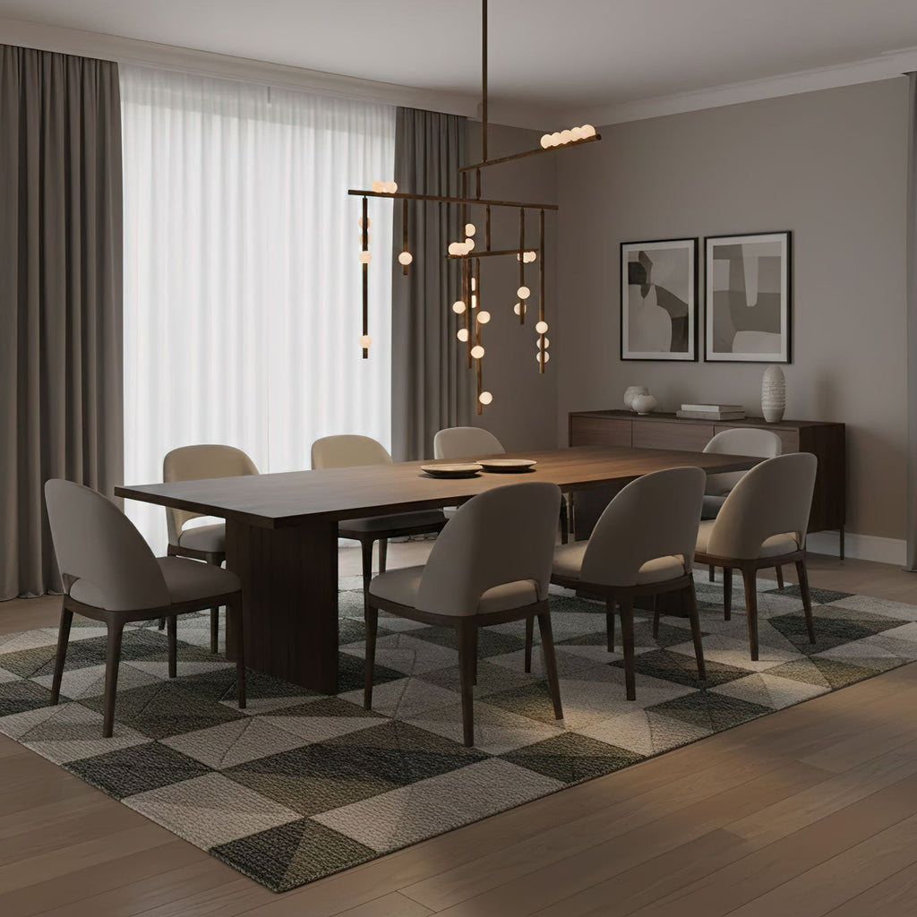 A Clérachic chandelier of thin brass bars and white orbs over a dark dining table in a grey room with long sheer curtains.