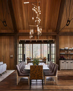 A Clérachic chandelier of brass rods and white orbs hangs high in a timber hall, over a long dining table with leather chairs.