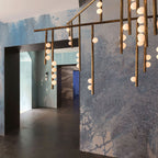 Close view of the brass bars and glowing white glass orbs on this Clérachic chandelier, seen against a blue textured wall.