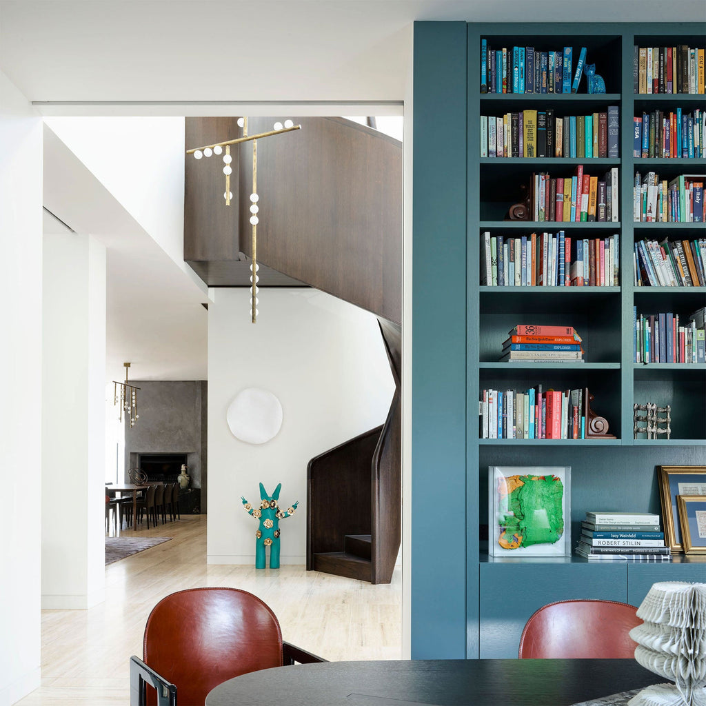 A Clérachic pendant seen from a landing in a white hallway with a teal bookcase, its brass rod and orbs hanging down the stairwell.