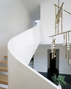 Beside a curving white staircase with timber treads, this Clérachic chandelier hangs its brass bars and white orbs through the stairwell.