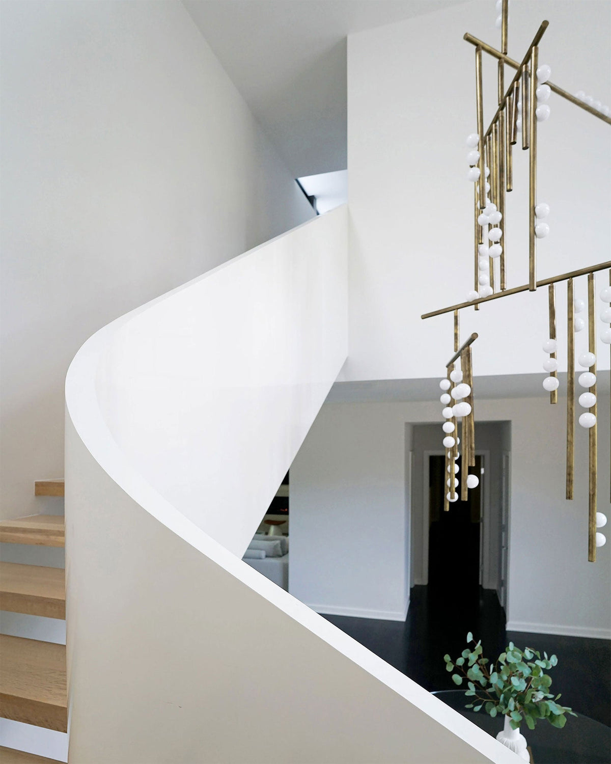 Beside a curving white staircase with timber treads, this Clérachic chandelier hangs its brass bars and white orbs through the stairwell.