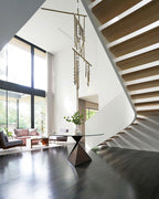 In a double-height room with a floating stair and a glass wall, a Clérachic chandelier hangs over a round table with a dark base.