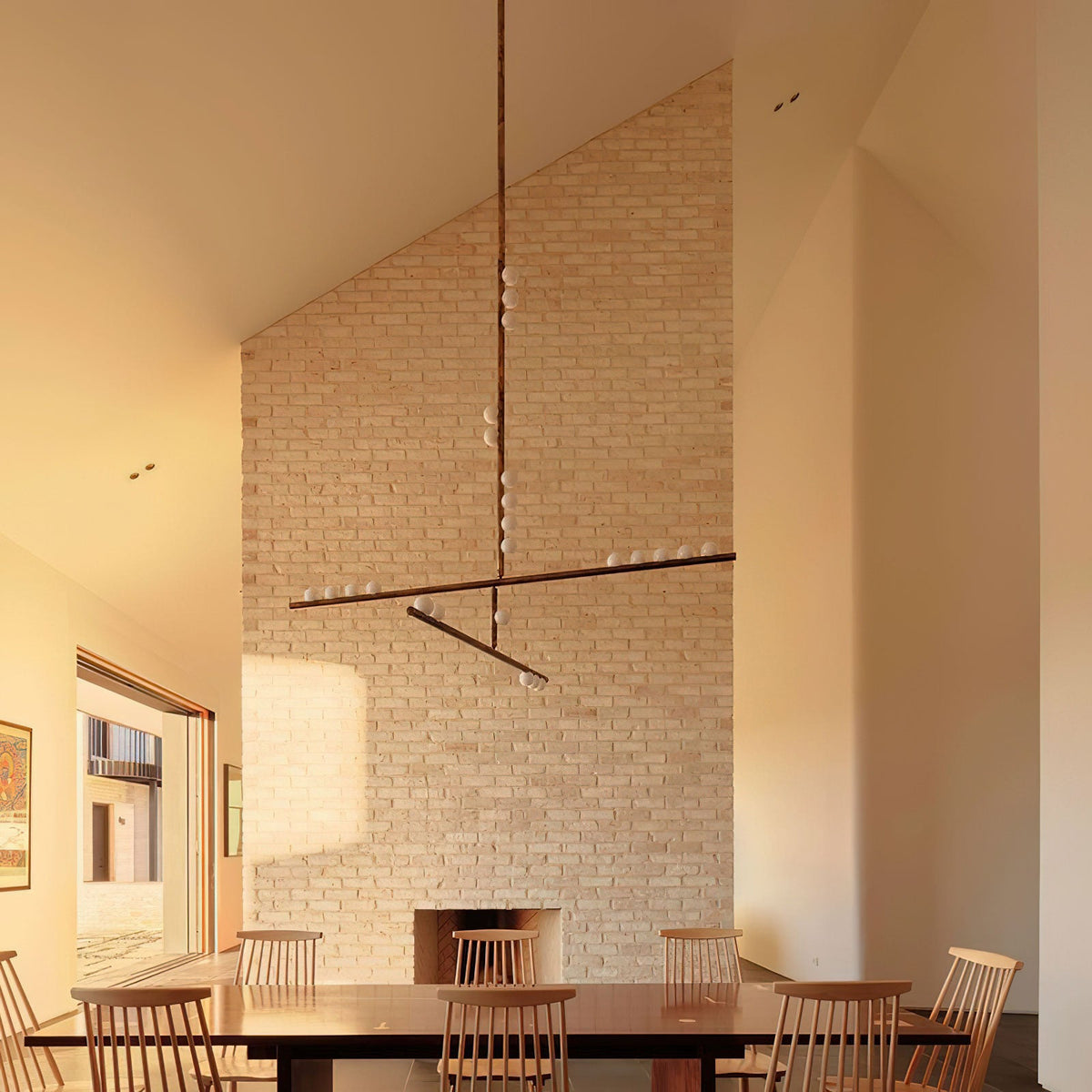 A Clérachic pendant with a long drop and crossed bars hangs by a tall brick wall, above a wooden dining table with spindle chairs.