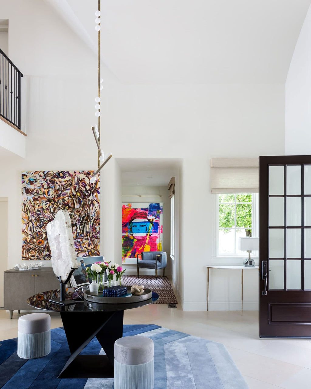 A tall Clérachic pendant with a column of white orbs hangs in a bright double-height hall with colourful art and a dark table.