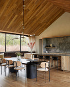 A Clérachic pendant with a long rod and white orbs hangs in a kitchen with a timber ceiling, above a black round dining table.