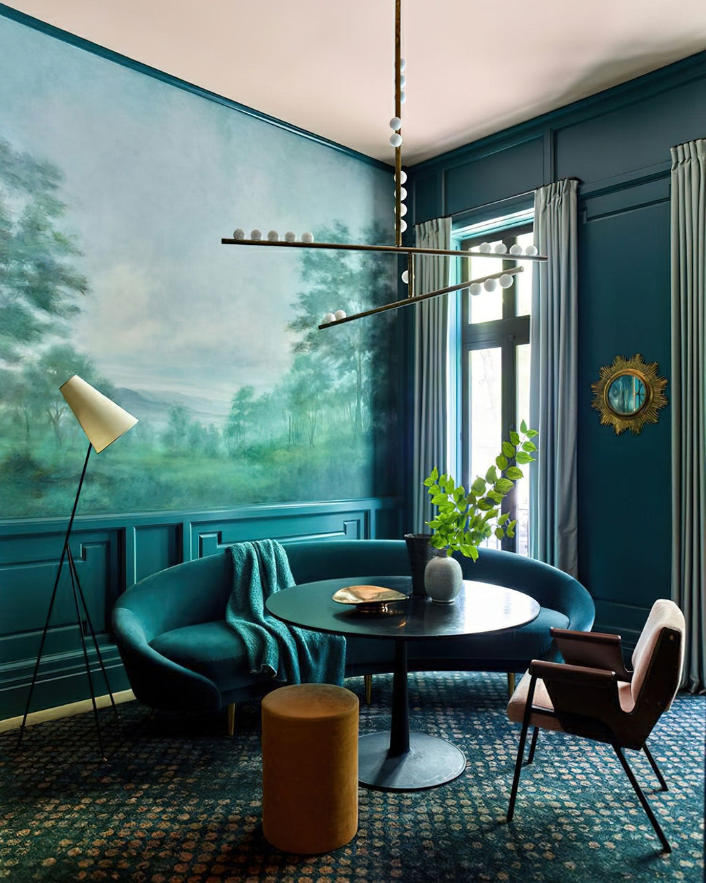 A Clérachic pendant with white orbs hangs in a teal room with a landscape mural, above a small round table and a green velvet sofa.