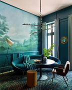 A Clérachic pendant with white orbs hangs in a teal room with a landscape mural, above a small round table and a green velvet sofa.
