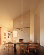 Above a long wooden table with spindle chairs, a Clérachic pendant hangs from a high ceiling against a pale brick wall.